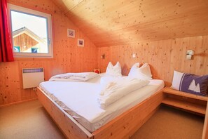 A wooden room with a bed, a window, and a wall-mounted heater.