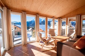A wooden interior with large windows, a wooden table, and a sofa. - Chalet in Hohentauern with an outdoor hot tub (Hohentauern)