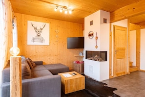 Un intérieur en bois comprenant un canapé, un téléviseur à écran plat, une cheminée et une porte donnant sur une autre pièce.