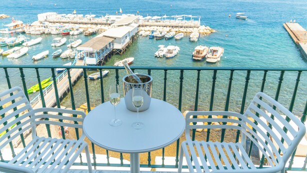 Ein Balkon mit weißen Stühlen und einem Tisch mit Blick auf eine Marina und zahlreichen dort liegenden Booten.
