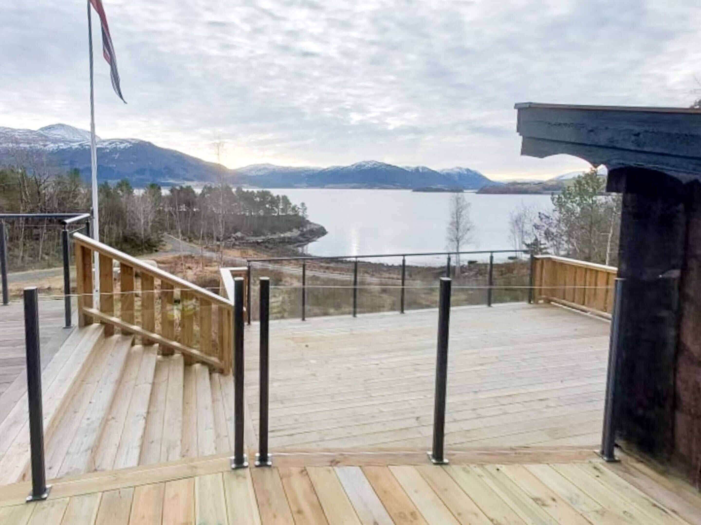 A wooden deck with a metal railing overlooking a lake and mountains.