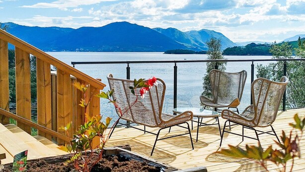A deck with wicker chairs and a wooden railing overlooking a lake with mountains in the background. - 5 Person Holiday Home in Oydegard (Tingvoll)