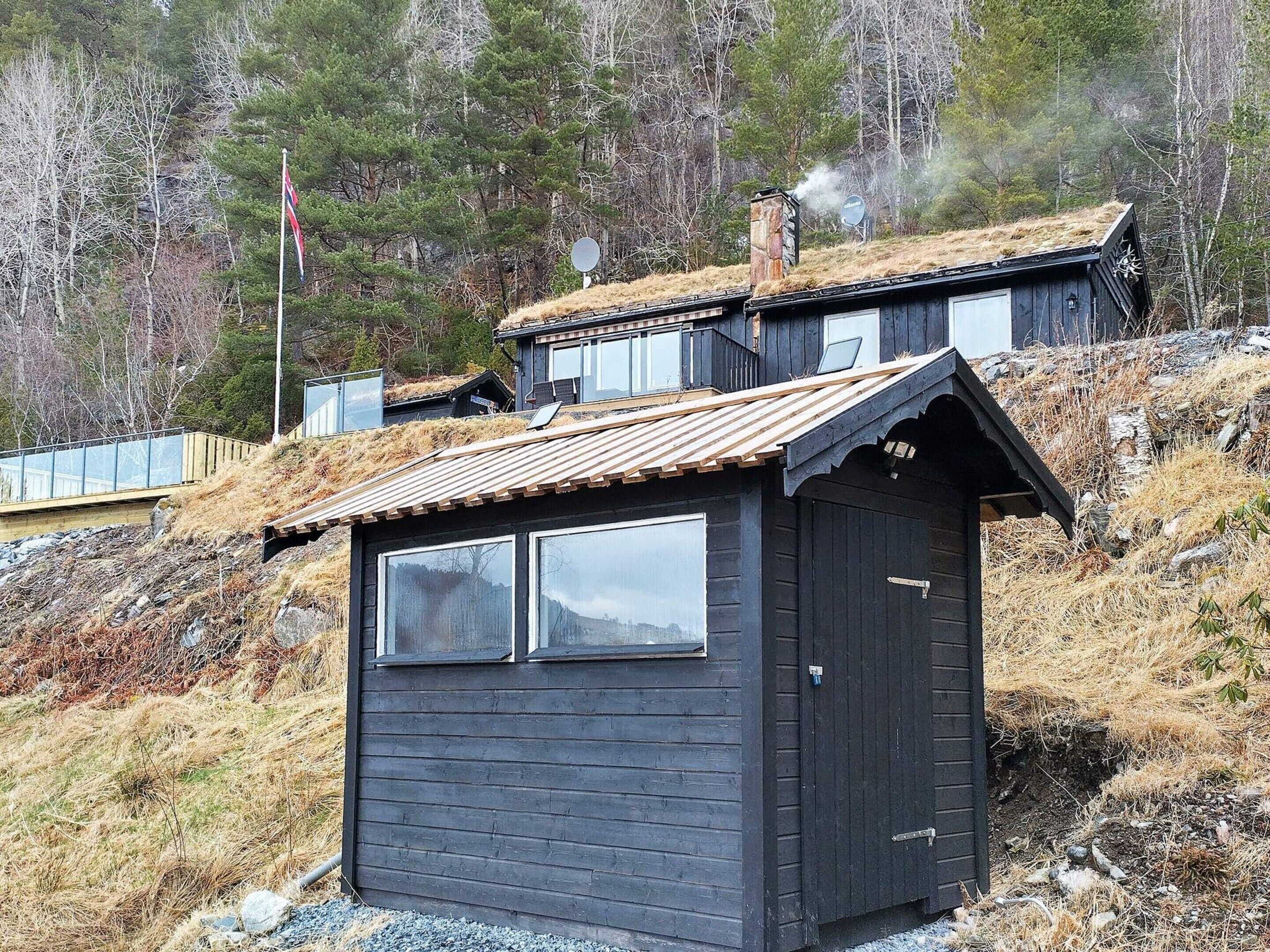 A small, dark wooden cabin with a sloped roof, a chimney, and a window.