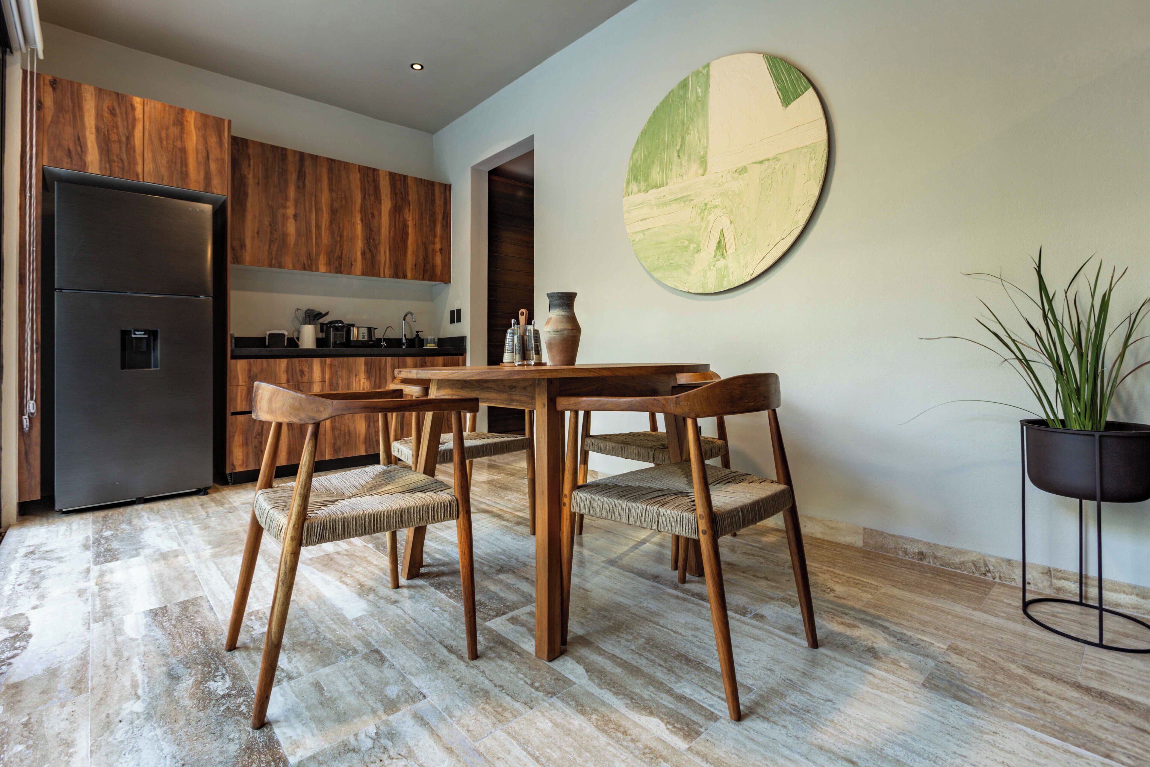 A modern kitchen with wooden cabinets, a dining table with chairs, a refrigerator, and a potted plant.