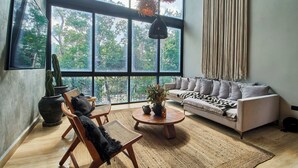 A spacious living room with a large window, a sofa, a coffee table, and a cactus plant. - BT Homes - Wellness Jungle (Tulum)