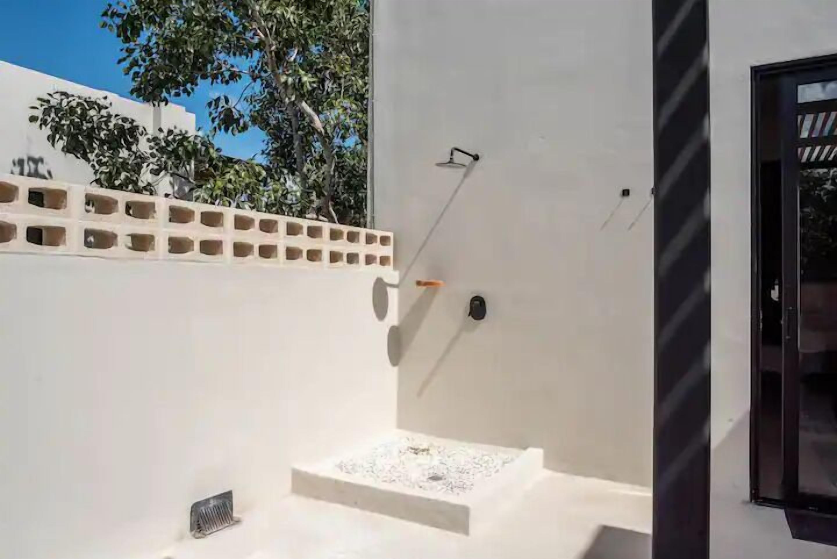 A modern outdoor shower area with a white wall, a small step, and a metal grate.