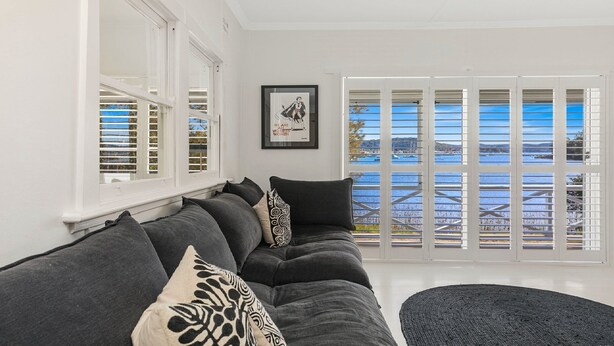 A living room with a dark grey sofa, patterned cushions, a framed artwork, and a view of the sea through large windows. - Yaringaa by HolidayCo. (HARDYS BAY)