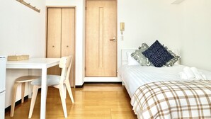 Une chambre à coucher comprenant un lit, une table de chevet et un bureau avec une chaise. Il y a deux portes, l’une donnant sur la salle de bain et l’autre sur la chambre.