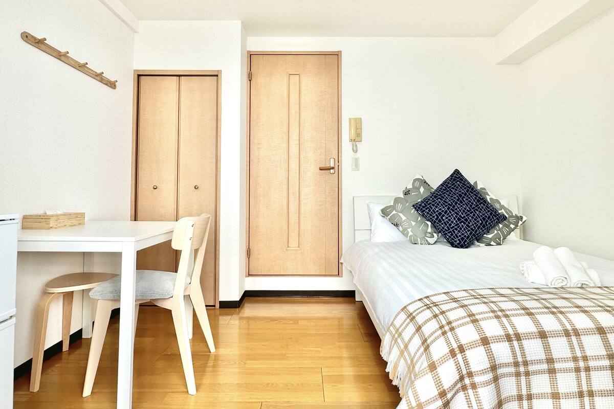 A bedroom with a bed, bedside table, and a desk with a chair. There are two doors, one leading to the bathroom and the other to the bedroom.