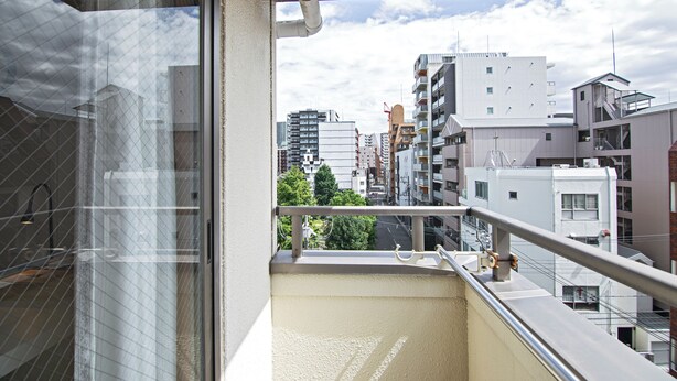 Un balcon donnant sur des immeubles urbains, avec une rambarde en métal et une porte en verre.