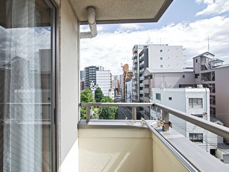Un balcón con vistas a edificios urbanos, una baranda metálica y un cerramiento de vidrio.