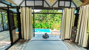 A bedroom with a large bed, a ceiling fan, and a view of a swimming pool. - 5 min to beach-private pool-great for couples (Dominicalito)