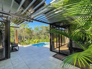 Un espacio al aire libre cubierto con piscina, mobiliario y plantas tropicales.