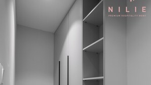 A hallway with a grey wall, a wooden floor, and a built-in grey shelving unit with black vertical dividers. - Arama Nilie Hospitality MGMT (Thessaloniki)