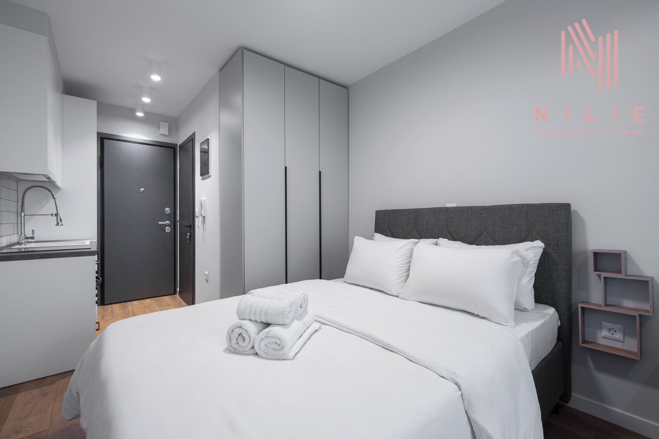 Een moderne hotelkamer met een net opgemaakt bed, een grijs hoofdeinde en een klein nachtkastje met een stopcontact.