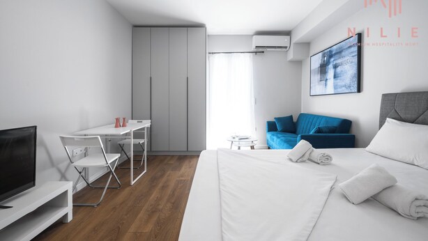 A modern hotel room with a bed, a desk, a TV, and a blue sofa. - Arama Nilie Hospitality MGMT (Thessaloniki)