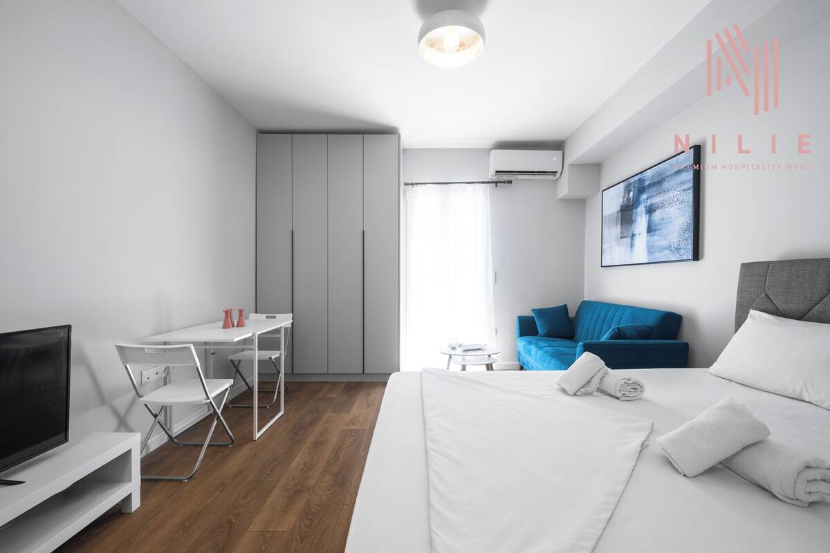 A modern hotel room with a bed, a desk, a TV, and a blue sofa.
