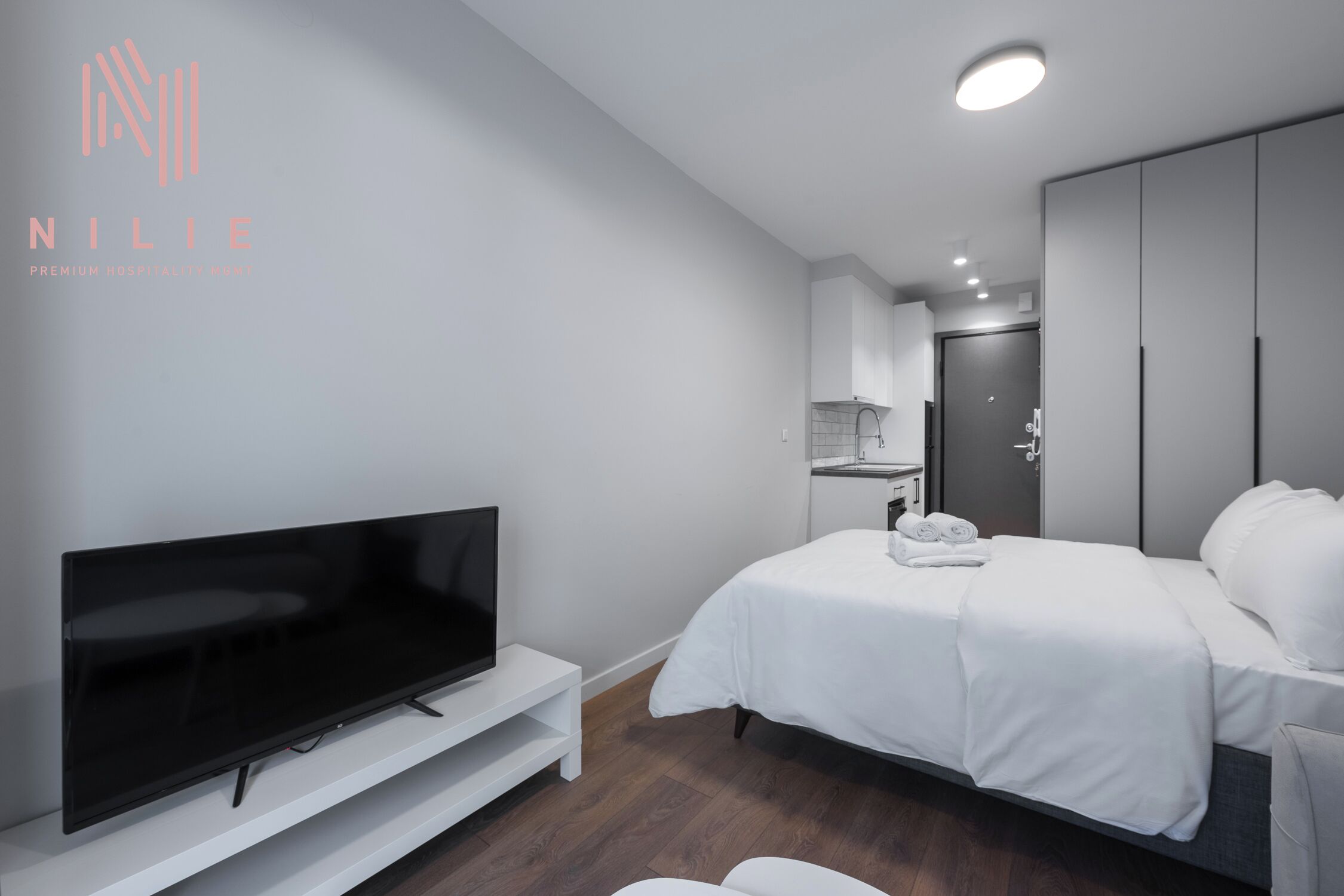 Een moderne hotelkamer met een flatscreen-tv, een bed met witte lakens, een kledingkast en een badkamer met handdoekhouder.