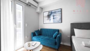 A modern hotel room with a blue sofa, a white chair, a bed, and a large abstract painting on the wall. - Arama Nilie Hospitality MGMT (Thessaloniki)