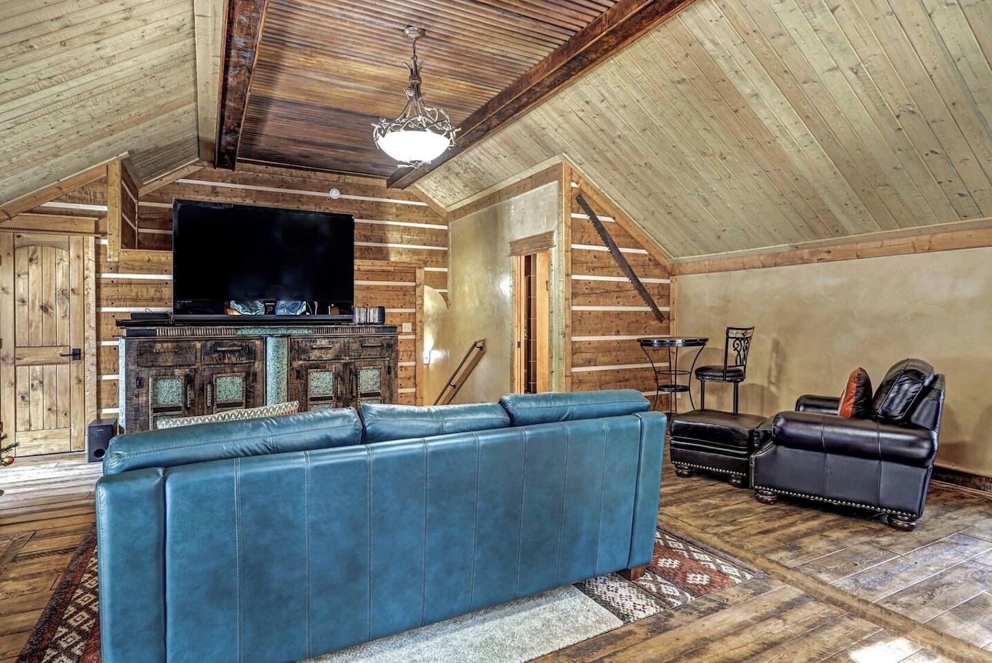 A spacious loft with a high ceiling, exposed wooden beams, a large blue leather sofa, a black leather recliner, a fireplace, and a television mounted on the wall.
