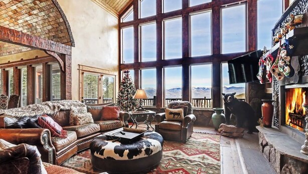A spacious living room with a fireplace, leather furniture, a Christmas tree, and a large window overlooking a mountainous landscape. - Spacious, Custom Built, Luxury Home Cabin with Hot Tub, Stunning Views,  (Angel Fire)