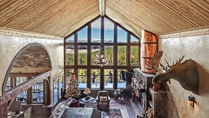 A spacious interior with a high ceiling, large windows offering mountain views, a fireplace with antlers, and a Christmas tree. - Spacious, Custom Built, Luxury Home Cabin with Hot Tub, Stunning Views,  (Angel Fire)