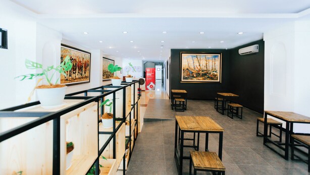 Un interior moderno con mesas y bancos de madera, plantas en macetas y obras de arte enmarcadas en las paredes.