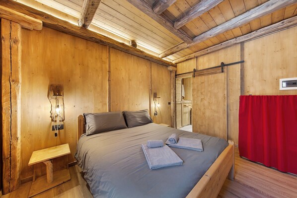 Une pièce en bois avec un lit, un banc et un rideau rouge.