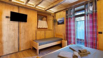 Una habitación de madera con una cama, una mesita, un televisor y una ventana con cortinas.