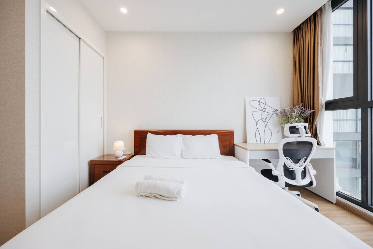 Ein Hotelzimmer mit einem großen Bett, einem Schreibtisch mit Stuhl, einem Nachttisch und einem Fenster mit Vorhängen.