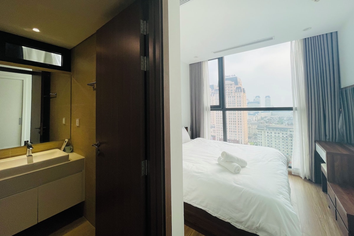 Ein Hotelzimmer mit Bett, Badezimmer mit Waschbecken und einem großen Fenster mit Blick auf die Stadt.