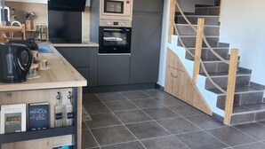 A modern kitchen with a built-in oven, microwave, and a wooden staircase leading to an upper level.