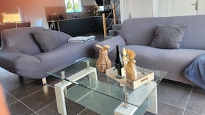 A modern living room with a grey sofa, a glass coffee table, and a kitchen in the background.