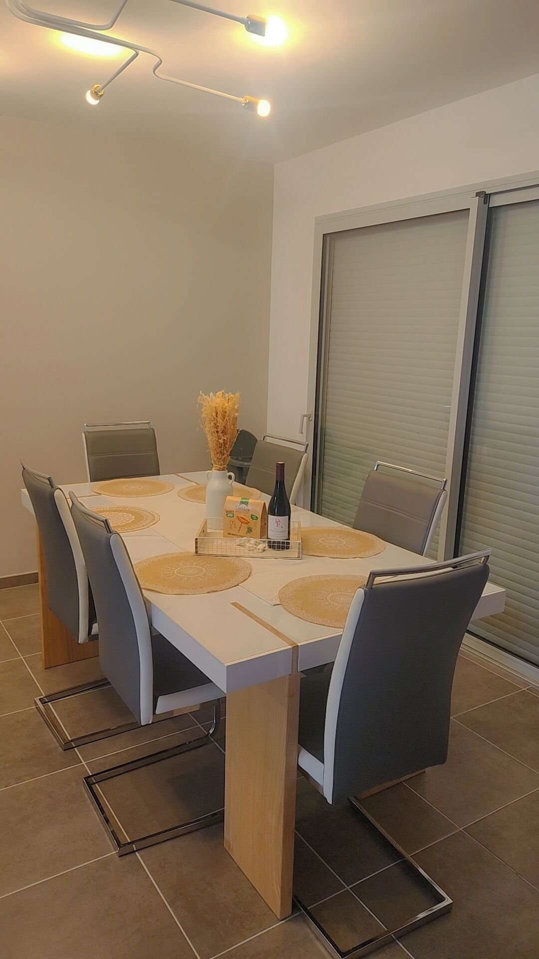 Een eetgedeelte met een witte tafel, grijze stoelen en een fles wijn.