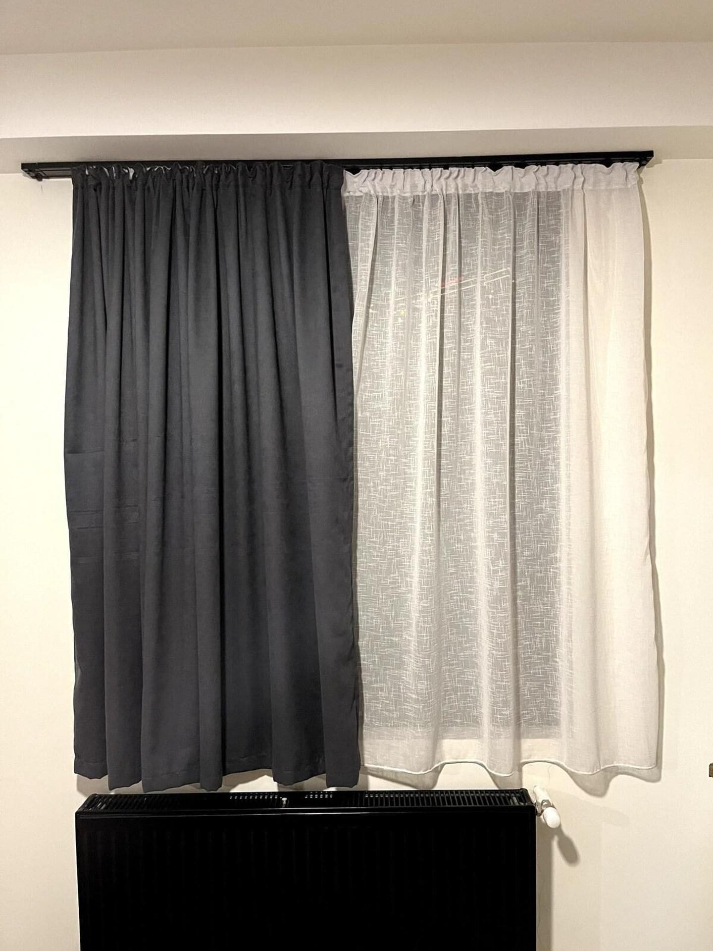 Una habitación con un radiador y dos cortinas, una oscura y otra clara.