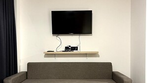 A modern living room with a grey sofa, a small black table, and a mounted TV on a white wall. - Gudauri - Apartment - Sleeps 4 - Pool - Parking (Kazbegi)