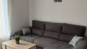 A modern living room with a grey sofa, a small wooden coffee table, and a potted plant. - 1A135 Comodo Apto 3 dormitorios (Gijón)