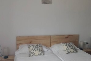 Un lit double avec une tête de lit en bois, deux oreillers ornés de motifs végétaux, une table de chevet avec une lampe et une prise électrique murale.