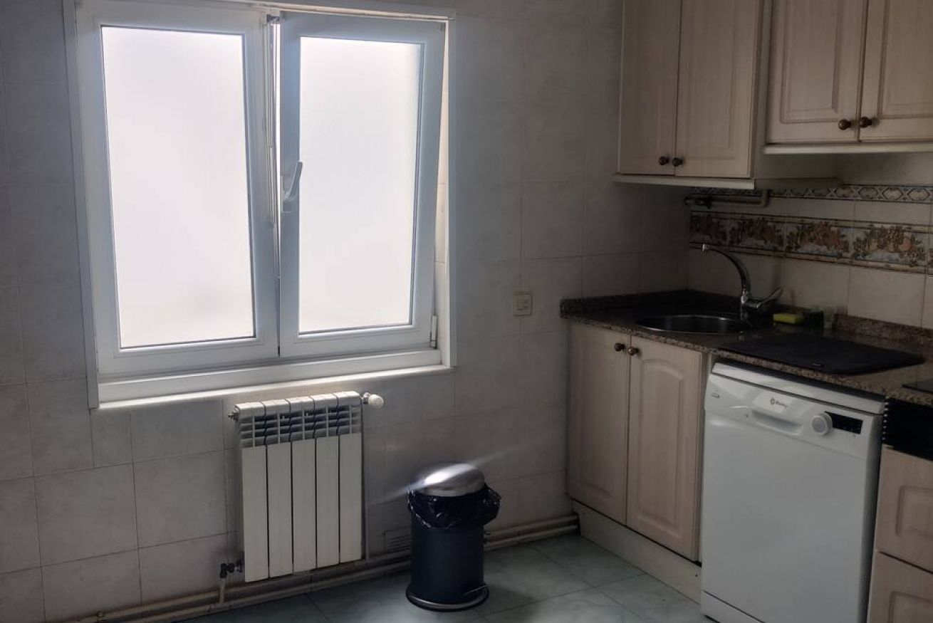 Eine Küche mit Fenster, Heizkörper, Geschirrspüler und Schränken.
