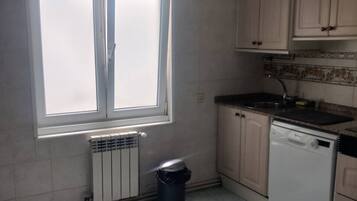 Eine Küche mit Fenster, Heizkörper, Geschirrspüler und Schränken.