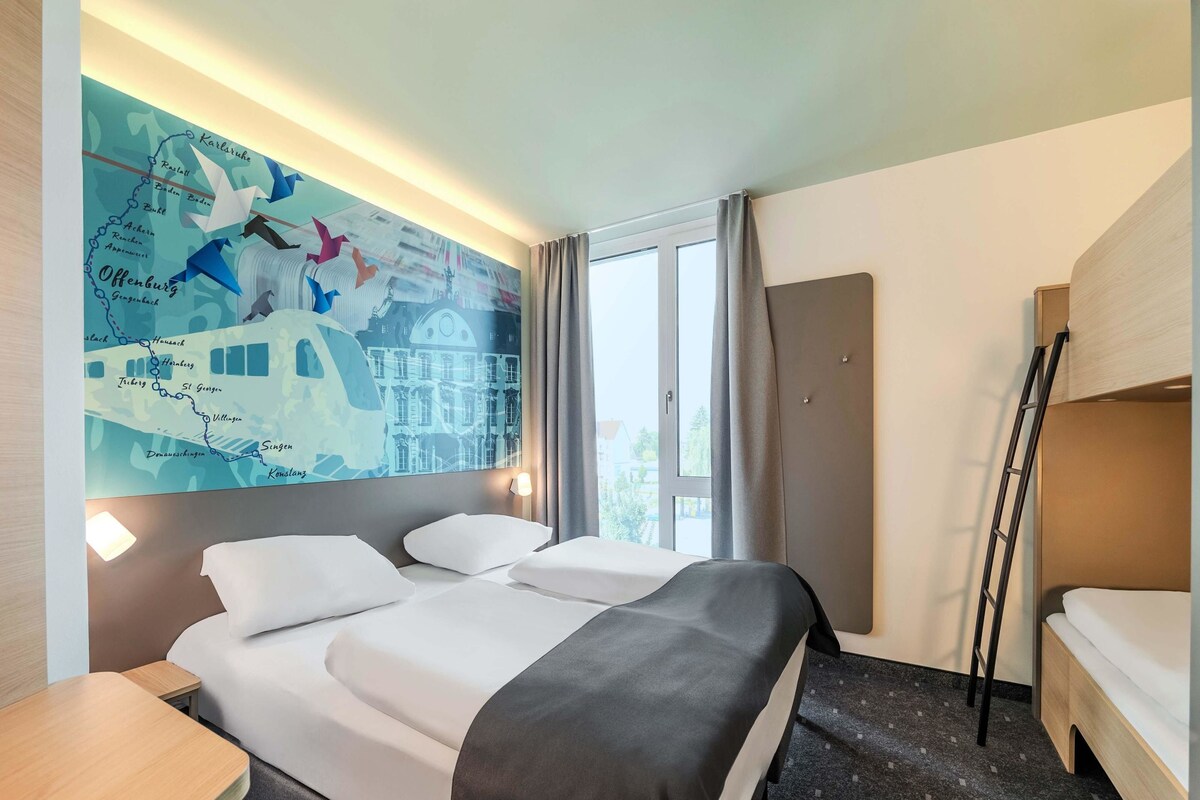 Een hotelkamer met een groot bed, een bureau, een kaart aan de muur en een raam met gordijnen.