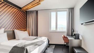 Habitación de hotel moderna con cama, escritorio, silla y un amplio ventanal con vistas a la ciudad.