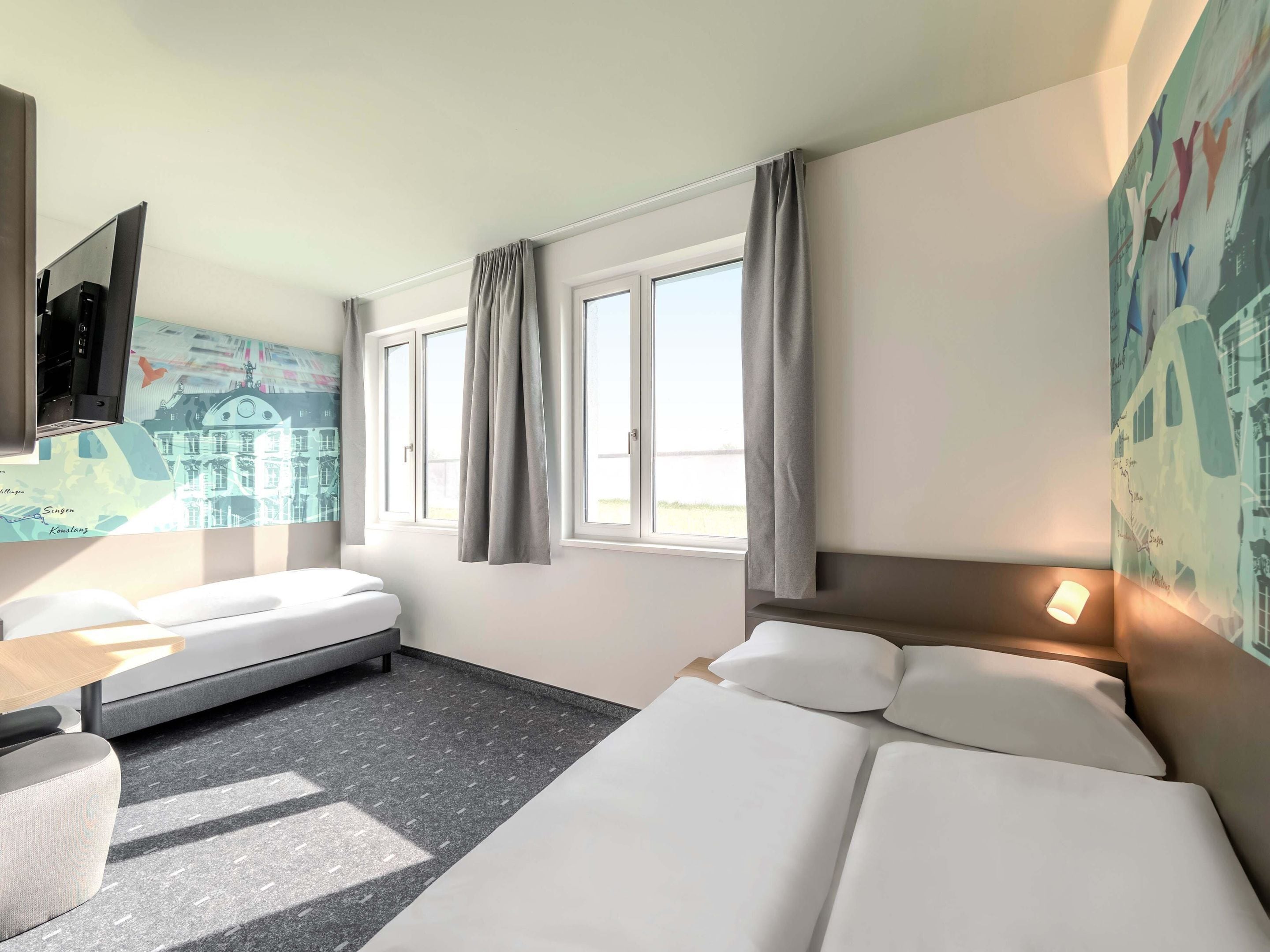 Camera d'albergo con un letto, una scrivania, una sedia, una televisione e una finestra con tende.