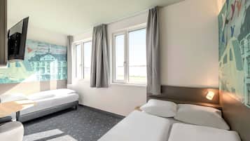 Ein Hotelzimmer mit Bett, Schreibtisch, Stuhl, Fernseher und einem Fenster mit Vorhängen.