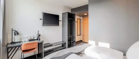 Une chambre d’hôtel moderne équipée d’un lit, d’un bureau, d’une chaise et d’un téléviseur fixé au mur.