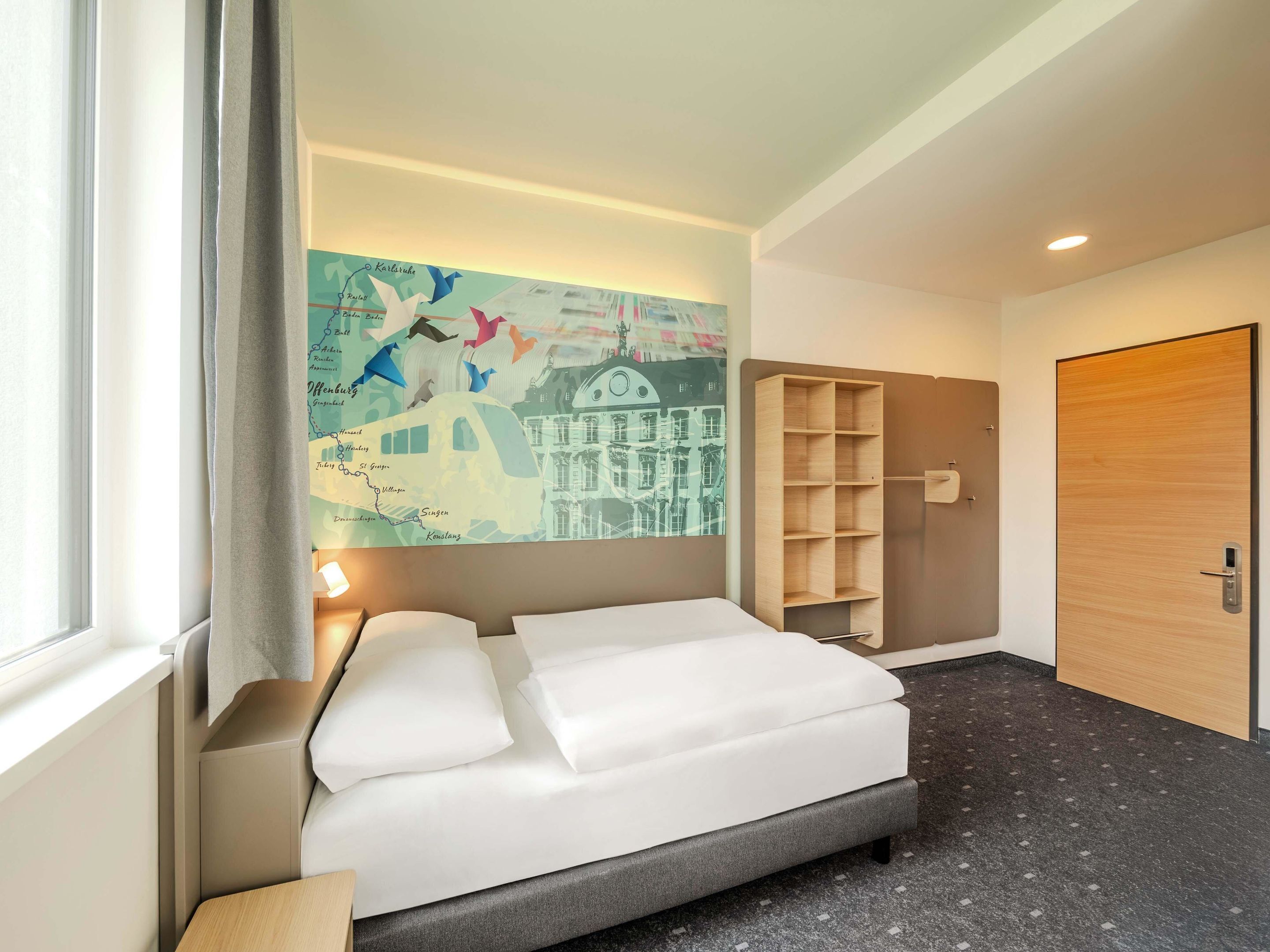 Una habitación de hotel con una cama, un mural de un mapa, un estante de madera y una puerta.