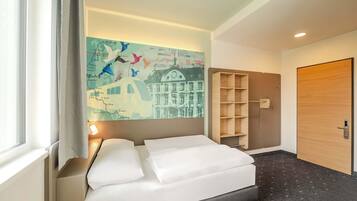 Una habitación de hotel con una cama, un mural de un mapa, un estante de madera y una puerta.