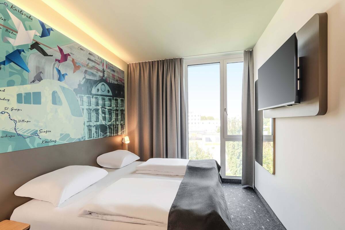 A hotel room with a bed, a desk, a TV, and a large window.