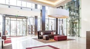 A spacious lobby with a modern design, featuring a large seating area with a sofa and ottoman, a reception desk, and a large window offering a view of the outside. - Hotel René Bohn (Ludwigshafen)