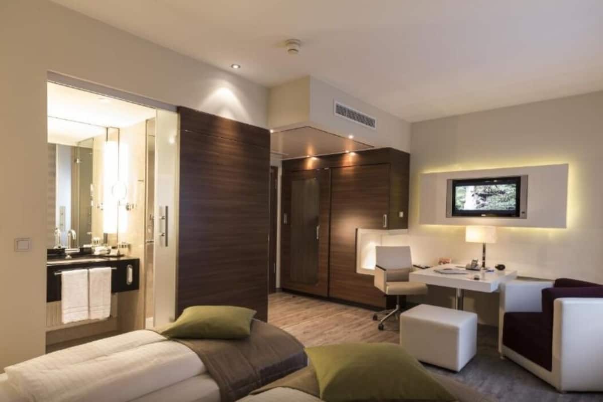 A modern hotel room with a bed, a desk, a chair, and a TV.